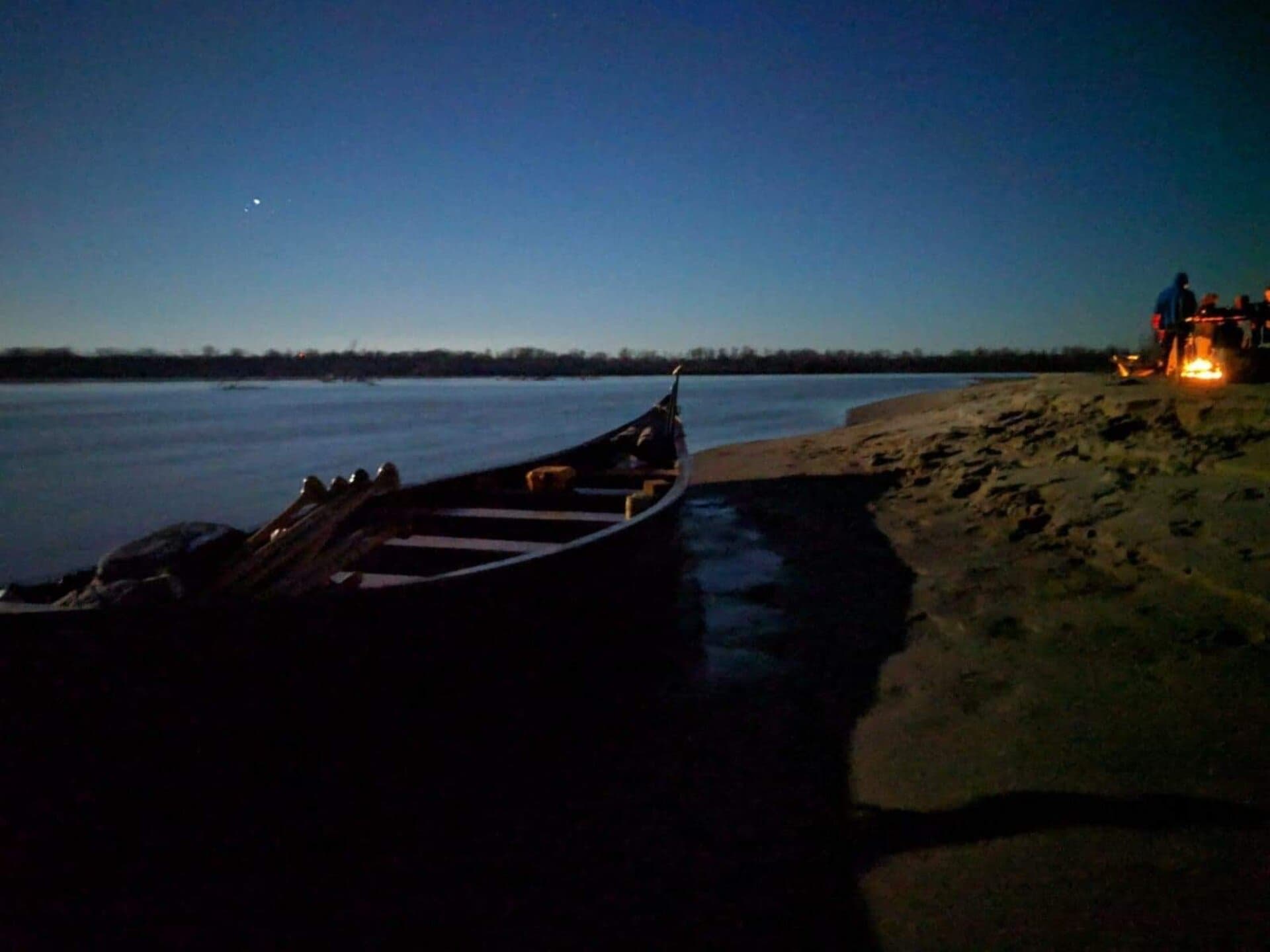 Quapaw voyageur canoe on the Mississippi at night with campfire